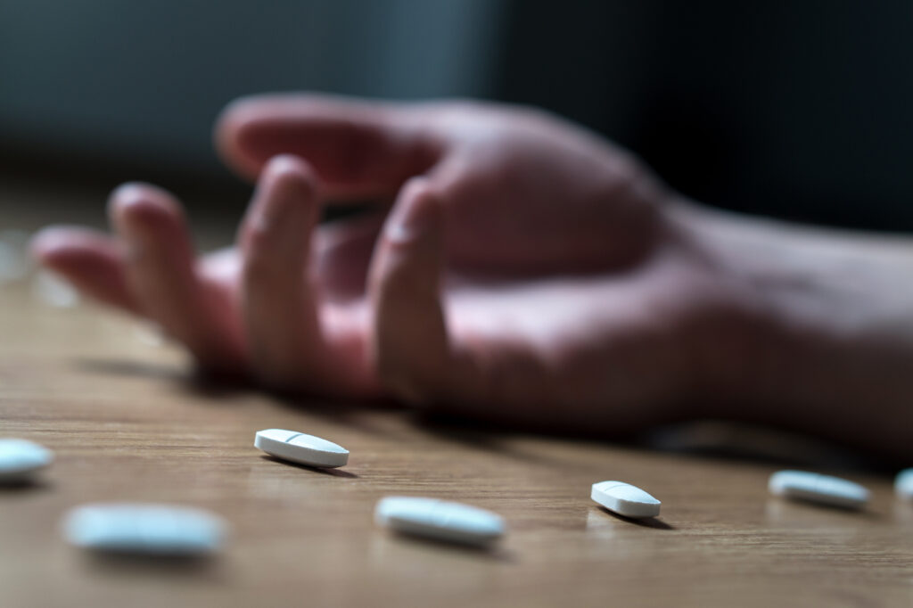 hand surrounded by many pills on the ground