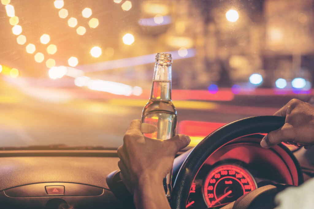 Person driving a car while holding a beer bottle