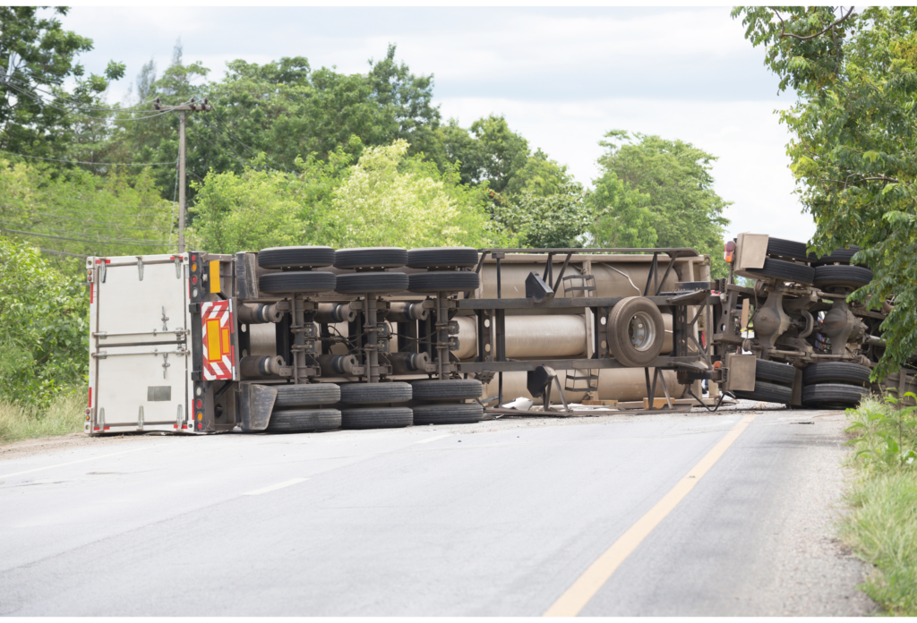 Overturned large truck lying across a rural road, blocking traffic with visible damage to the vehicle