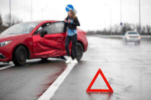 Driver sitting at roadside after traffic accident. Focus is on the red triangle sign
