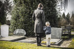 woman and child mourn the loss of a loved one at their grave site.